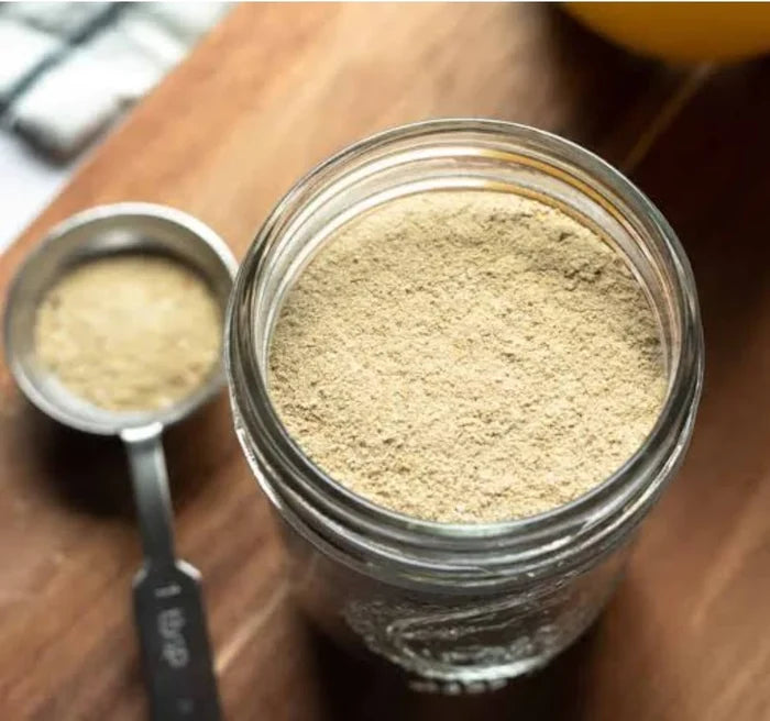 Overhead view of beef bone broth powder in a glass jar next to a measuring spoon on a wooden board