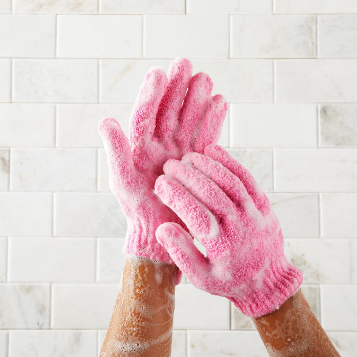 Hands wearing sudsy pink exfoliating dog washing gloves against a tiled shower wall