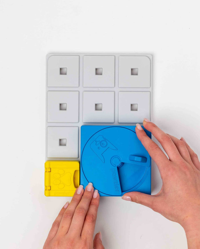Hands attaching a blue spinning piece and yellow piece to a white Pawzler Base Pawzle tray