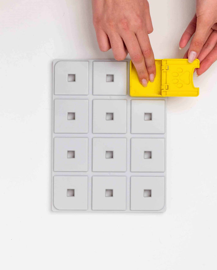 Hands attaching a yellow paw-shaped piece to a white Pawzler Base Pawzle tray
