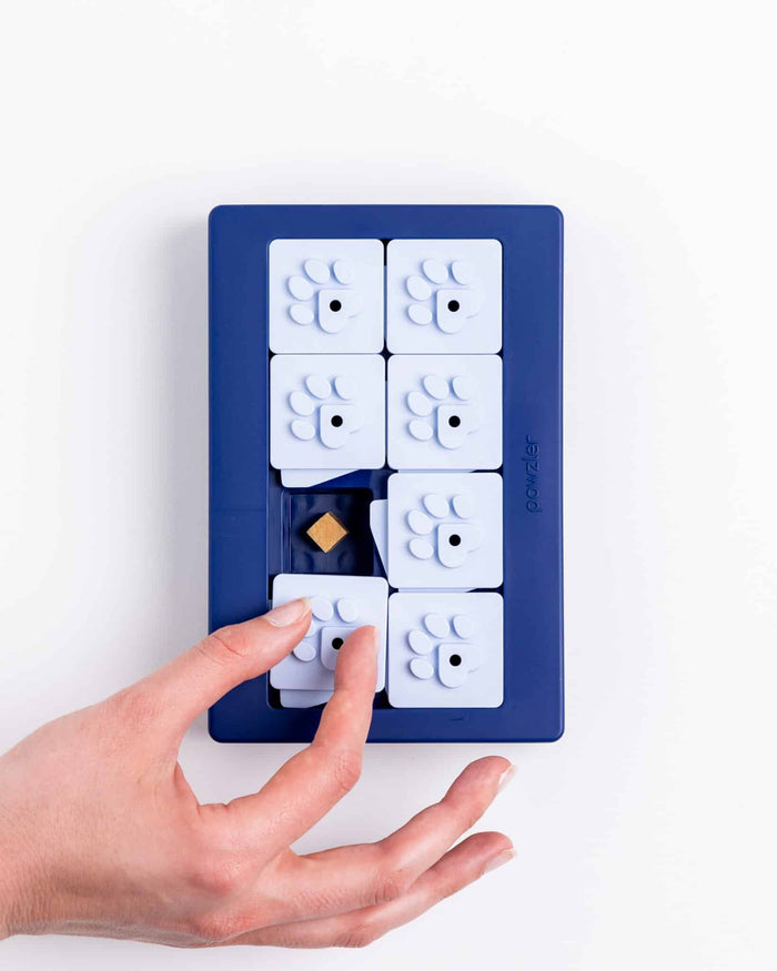 Hand sliding a white paw-print tile on the navy blue Pawzler Louvre puzzle tray
