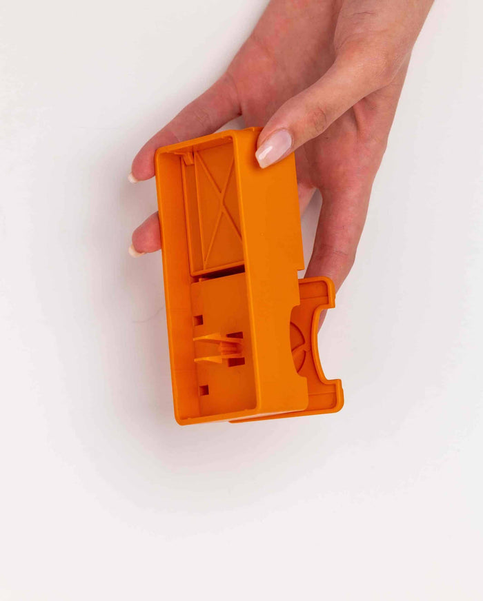 Hand holding the orange Pawzler Maya puzzle piece, showing its hinged compartment