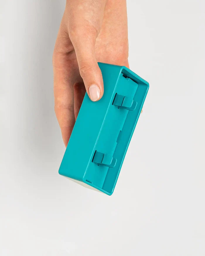 Hand holding the teal Pawzler Nai puzzle piece, showing its underside attachment