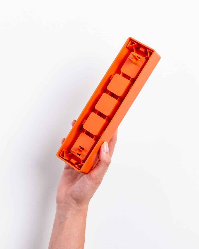 Hand holding the orange Pawzler Zhu puzzle piece, showing its underside attachment slots