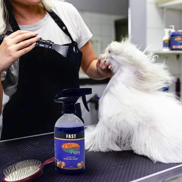 Groomer with a fluffy white dog on the table beside the Plush Puppy FAST trigger spray bottle